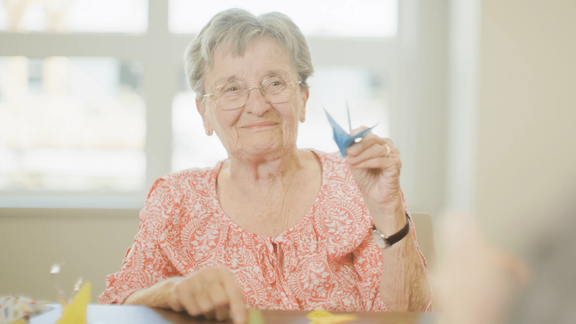 An elderly woman making paper origami birds in her senior home