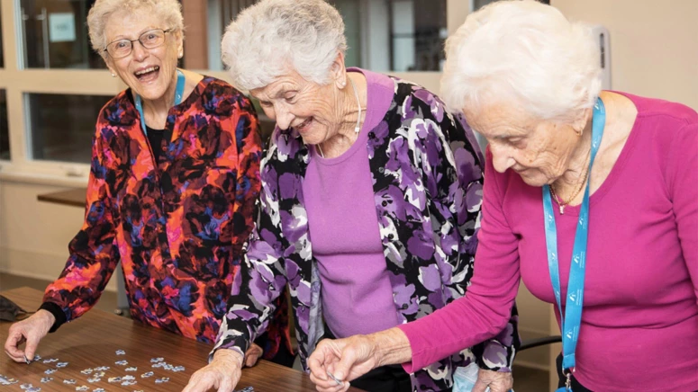 Three senior women wearing bright colors and building a puzzle