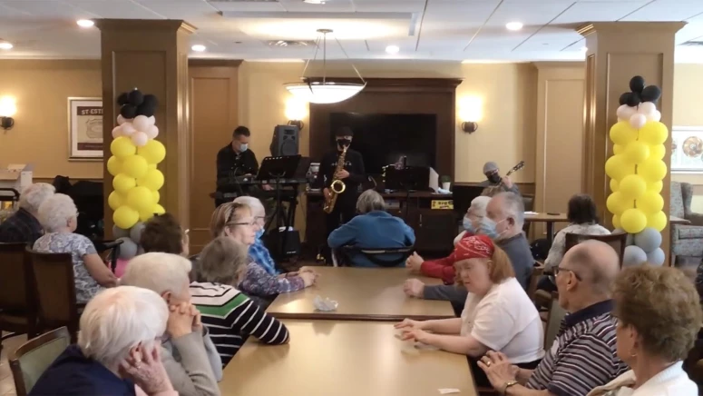 A group of seniors sitting around a table listening to live music in their senior home